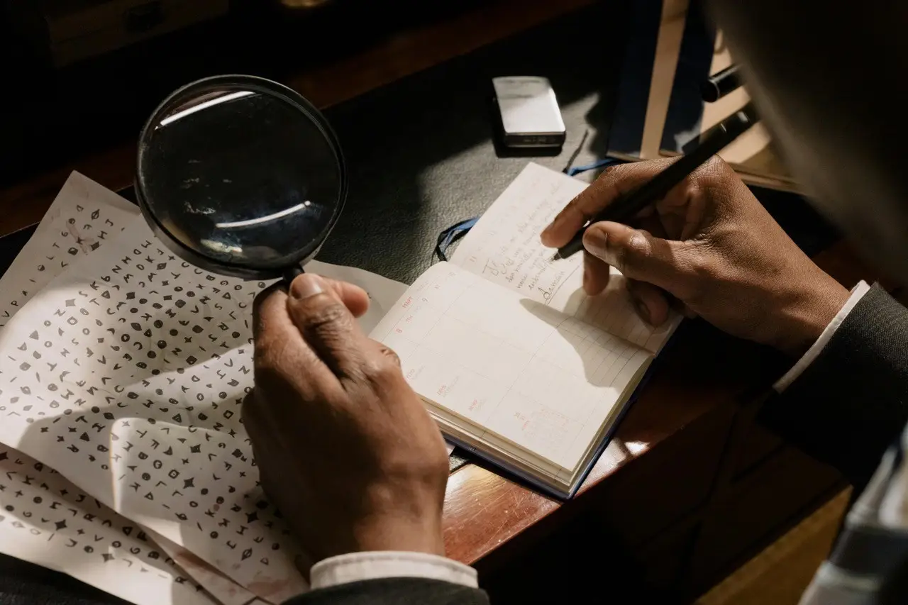 Man writing something on book and magnifying glass in other hand